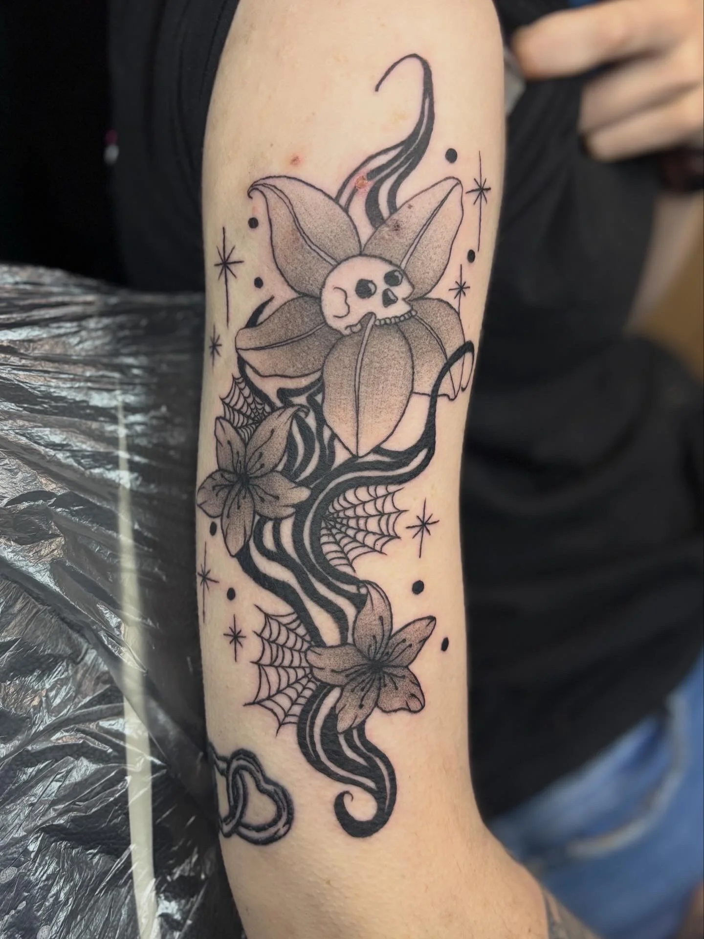 Black and grey neo-traditional skull lily with spider webs on forearm