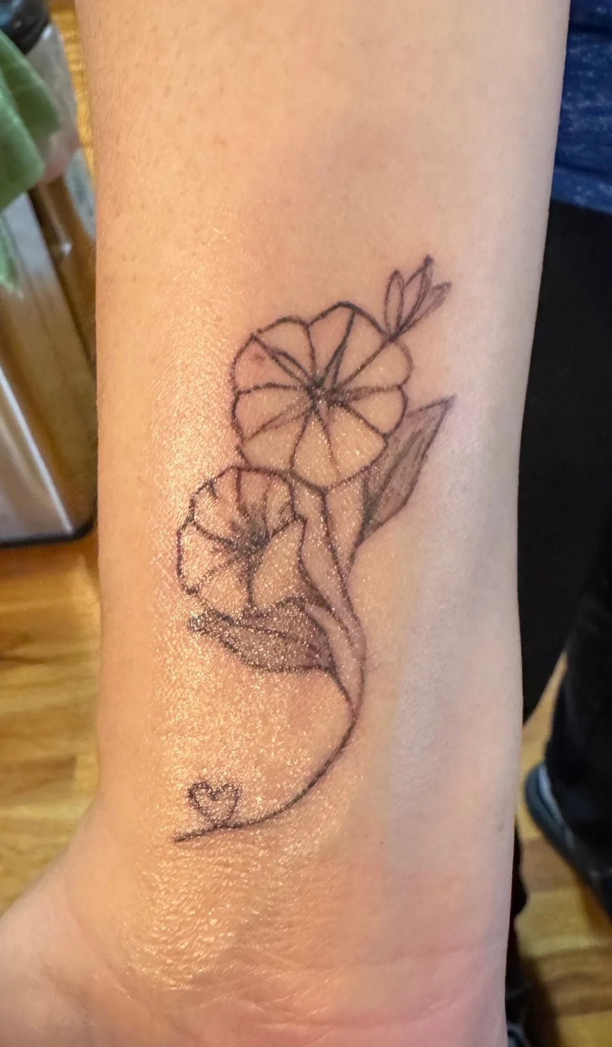 Fine line botanical flower tattoo with vine detail on wrist