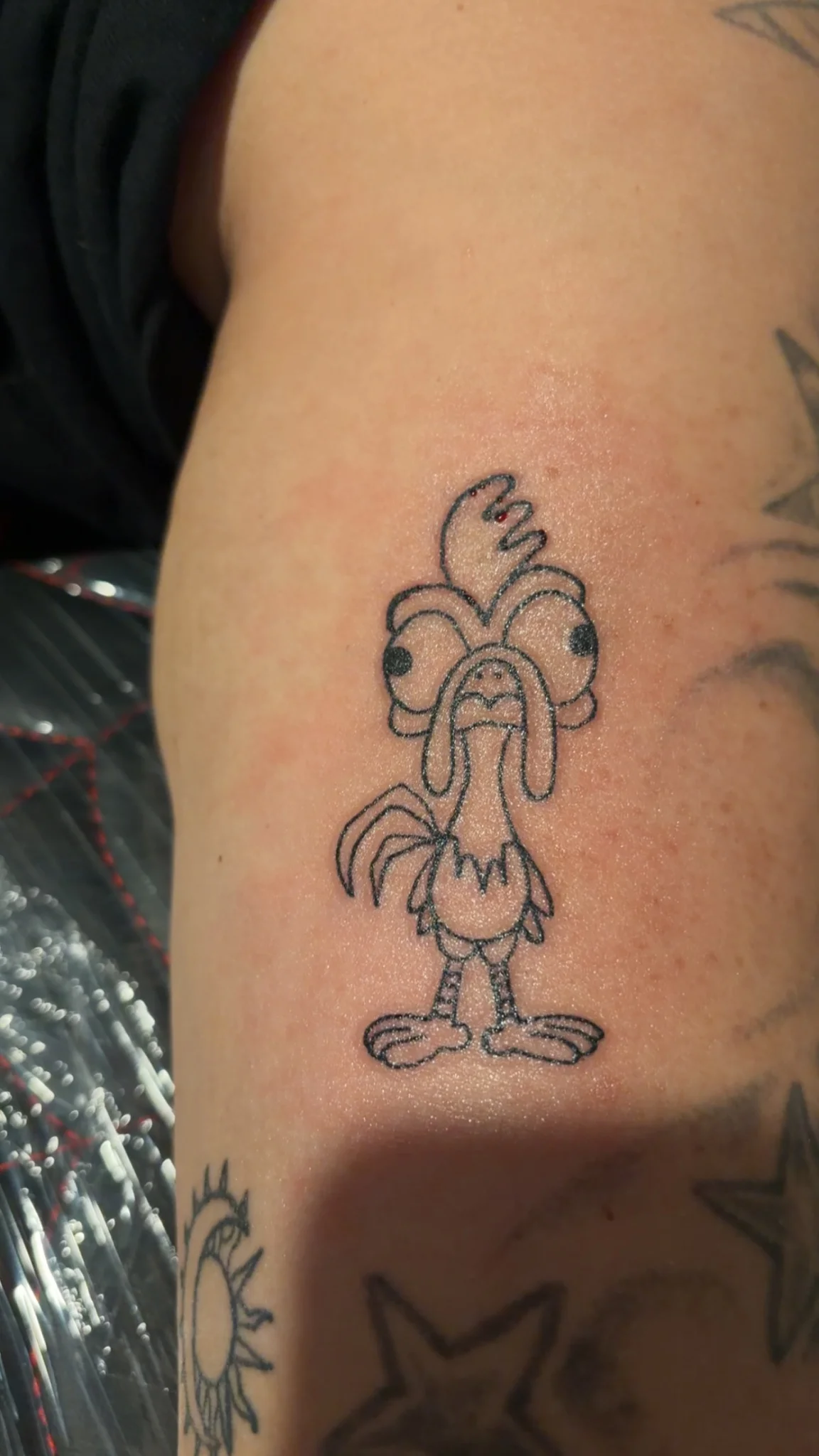 Illustrative cartoon rooster outline tattoo on upper arm