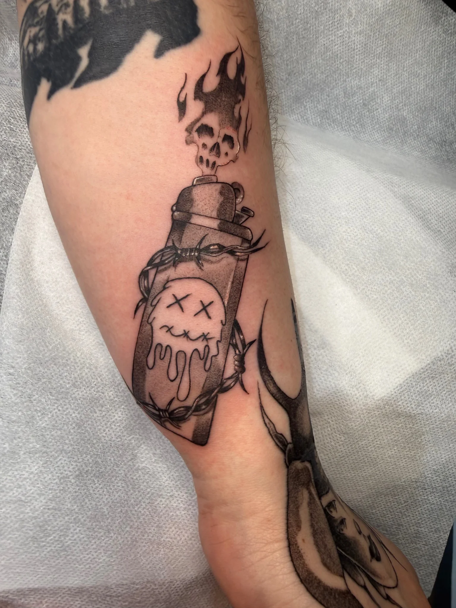Black and grey lighter tattoo with skull smoke and barbed wire on forearm