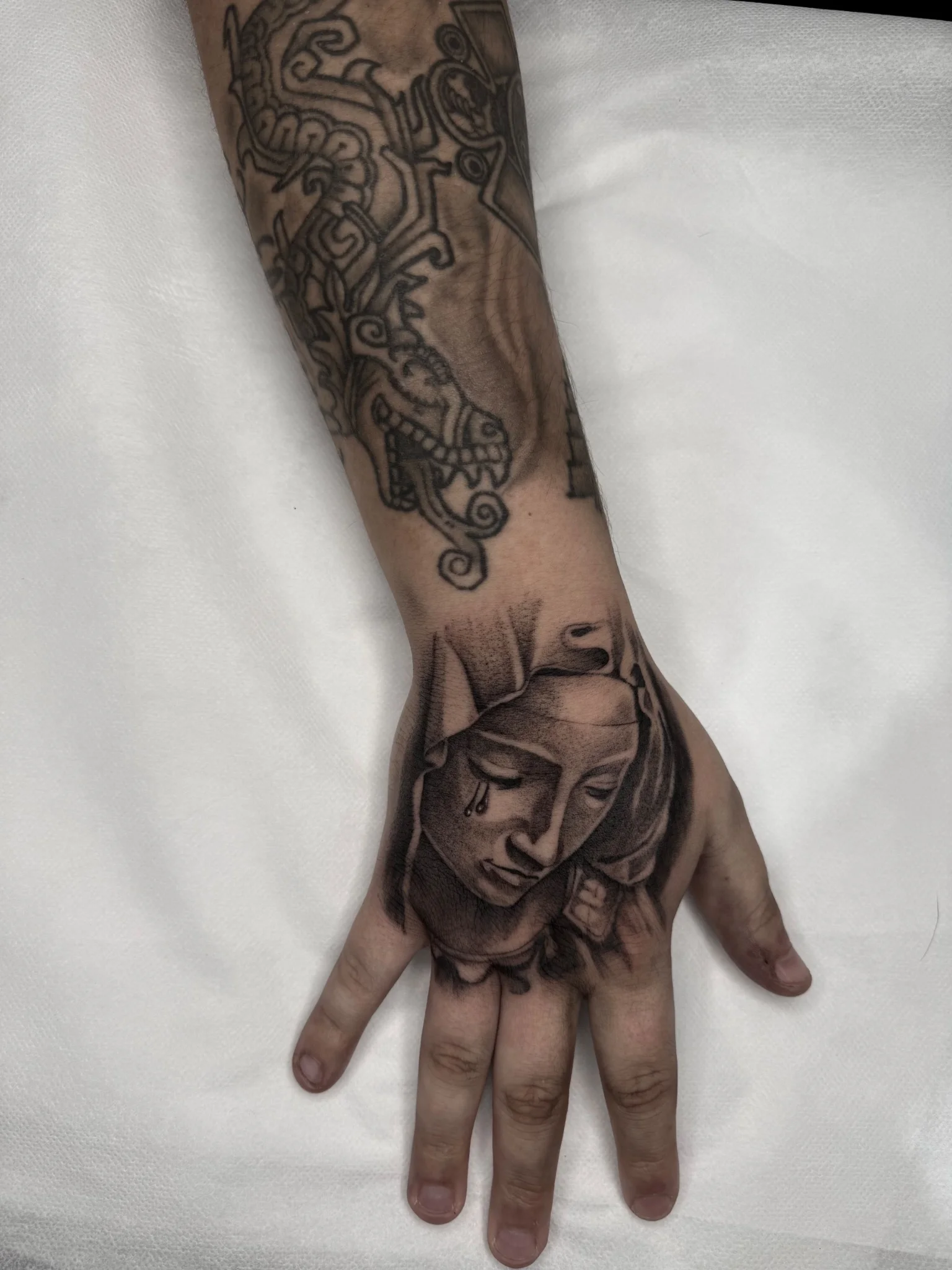 Black and grey realism weeping Virgin Mary tattoo on hand and forearm