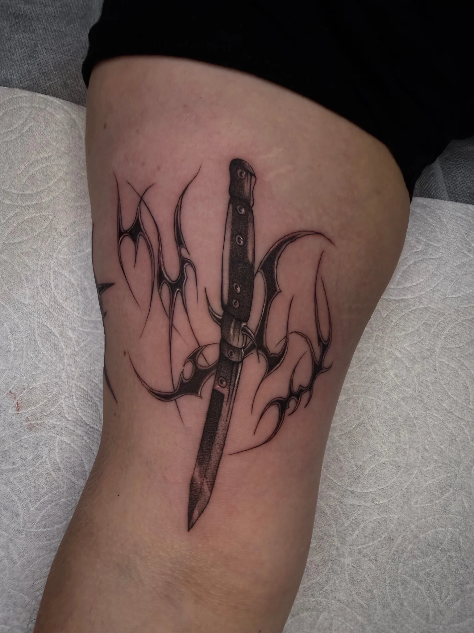 Black and grey butterfly knife with tribal lettering on thigh