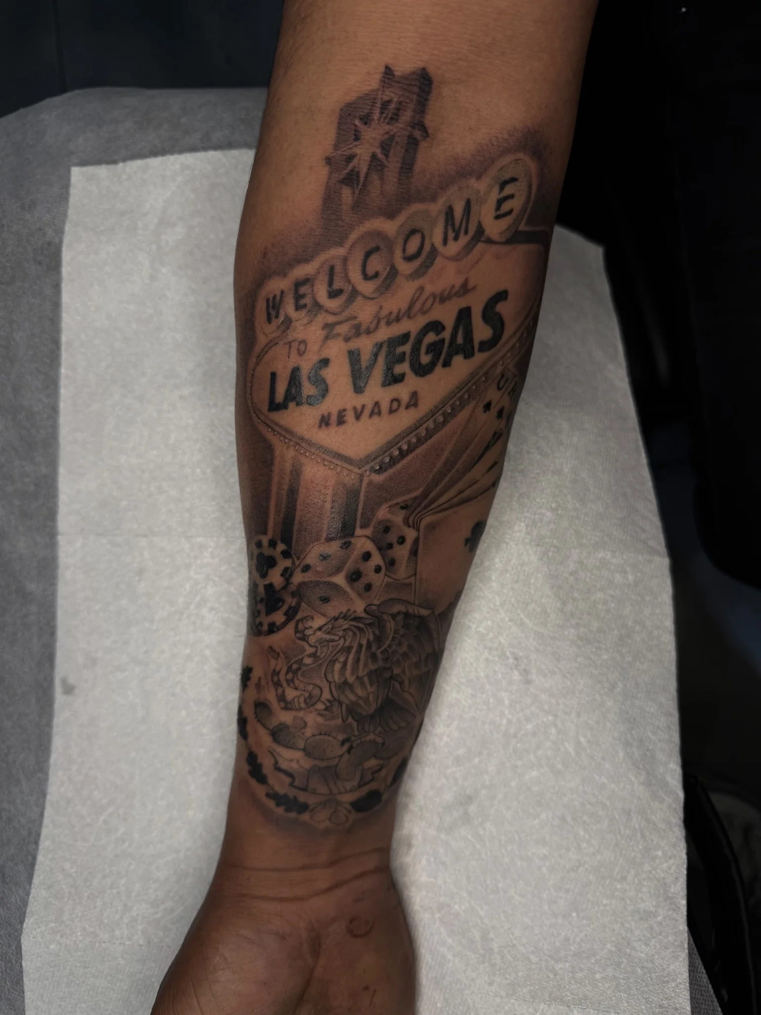 Black and grey Las Vegas sign tattoo with dice and cards on forearm
