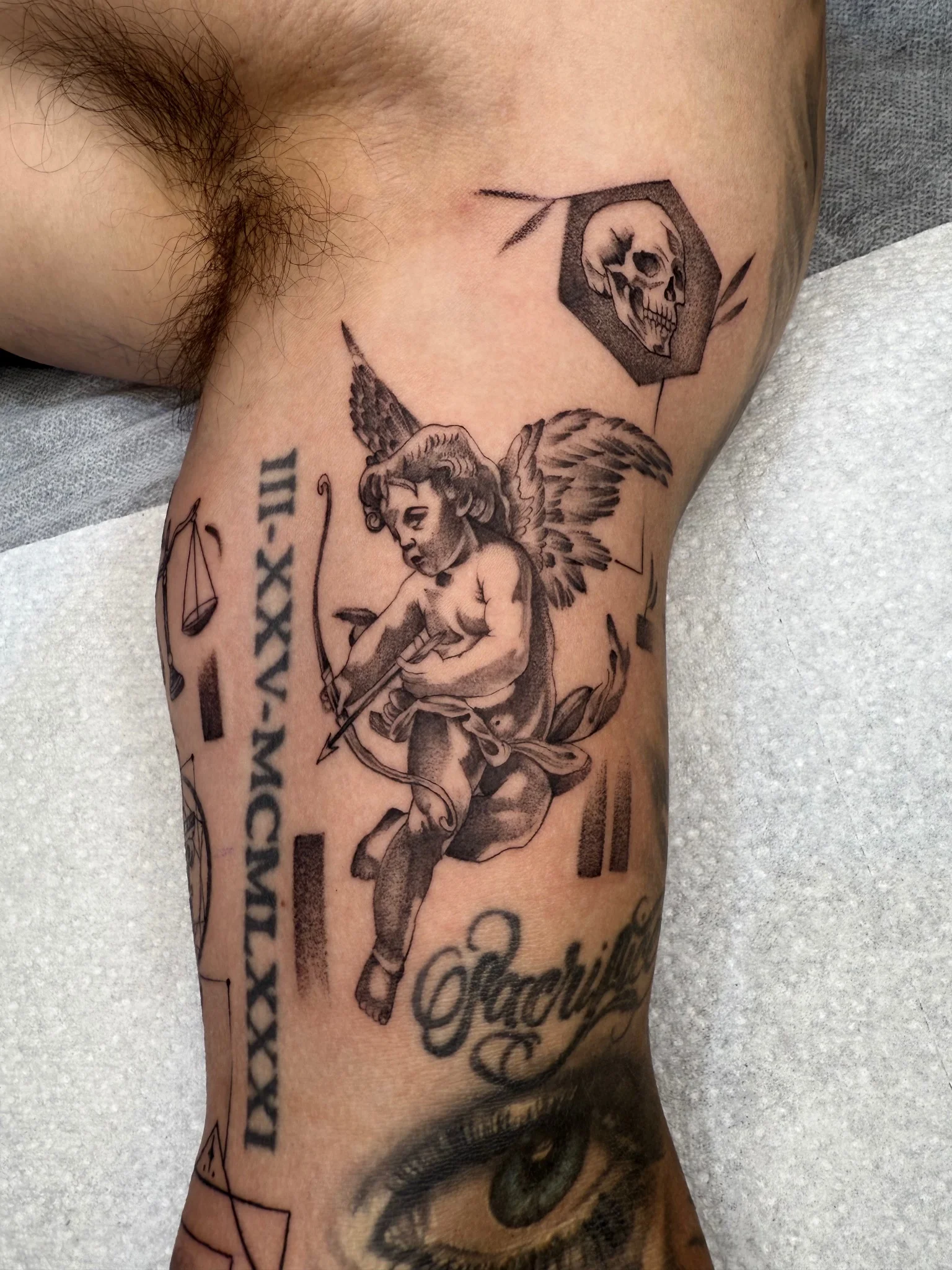 Black and grey cherub, skull, and script tattoo on knee and leg