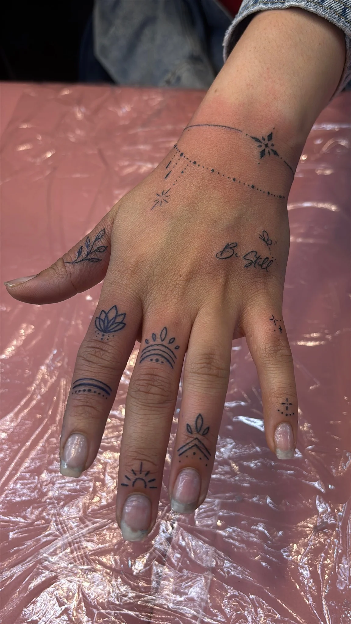 Fine line hand and finger tattoos with script, botanicals, and celestial motifs