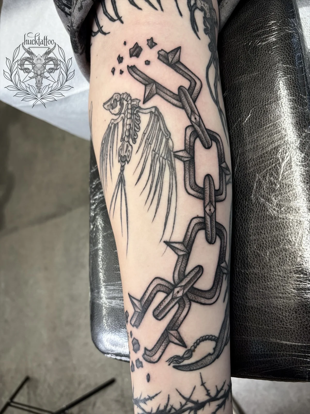Illustrative skeleton bird with chains tattoo on forearm