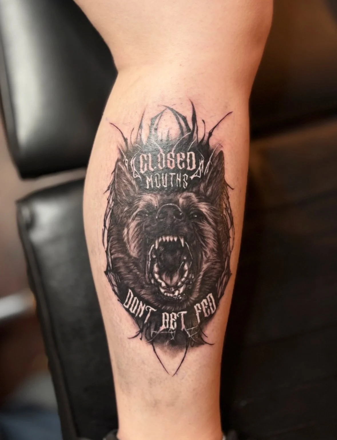 Black and grey realistic wolf with lettering tattoo on calf