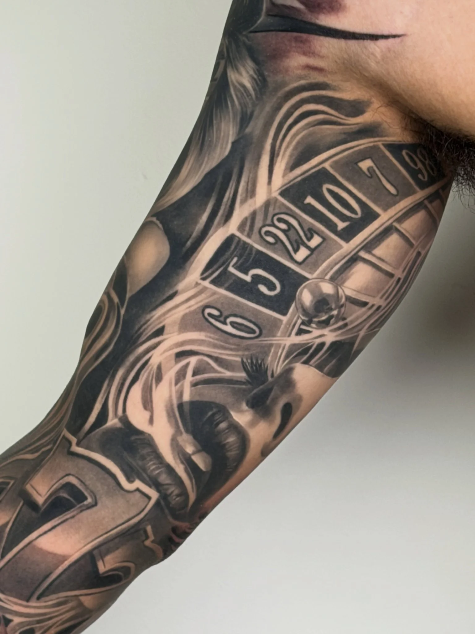 Black and grey realism casino sleeve tattoo with roulette wheel and female face