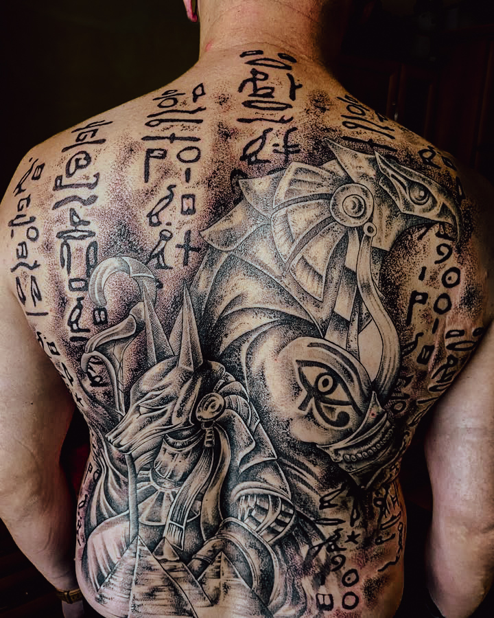 Large-scale Egyptian mythology back tattoo featuring hieroglyphic text and deity imagery