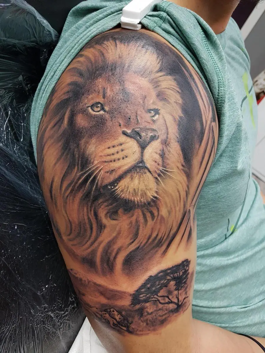 Realistic lion head portrait tattoo on upper arm with landscape base