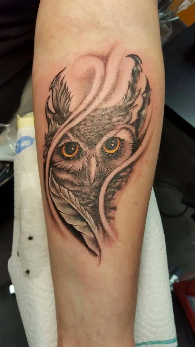 Black and grey realistic owl with golden eyes on forearm