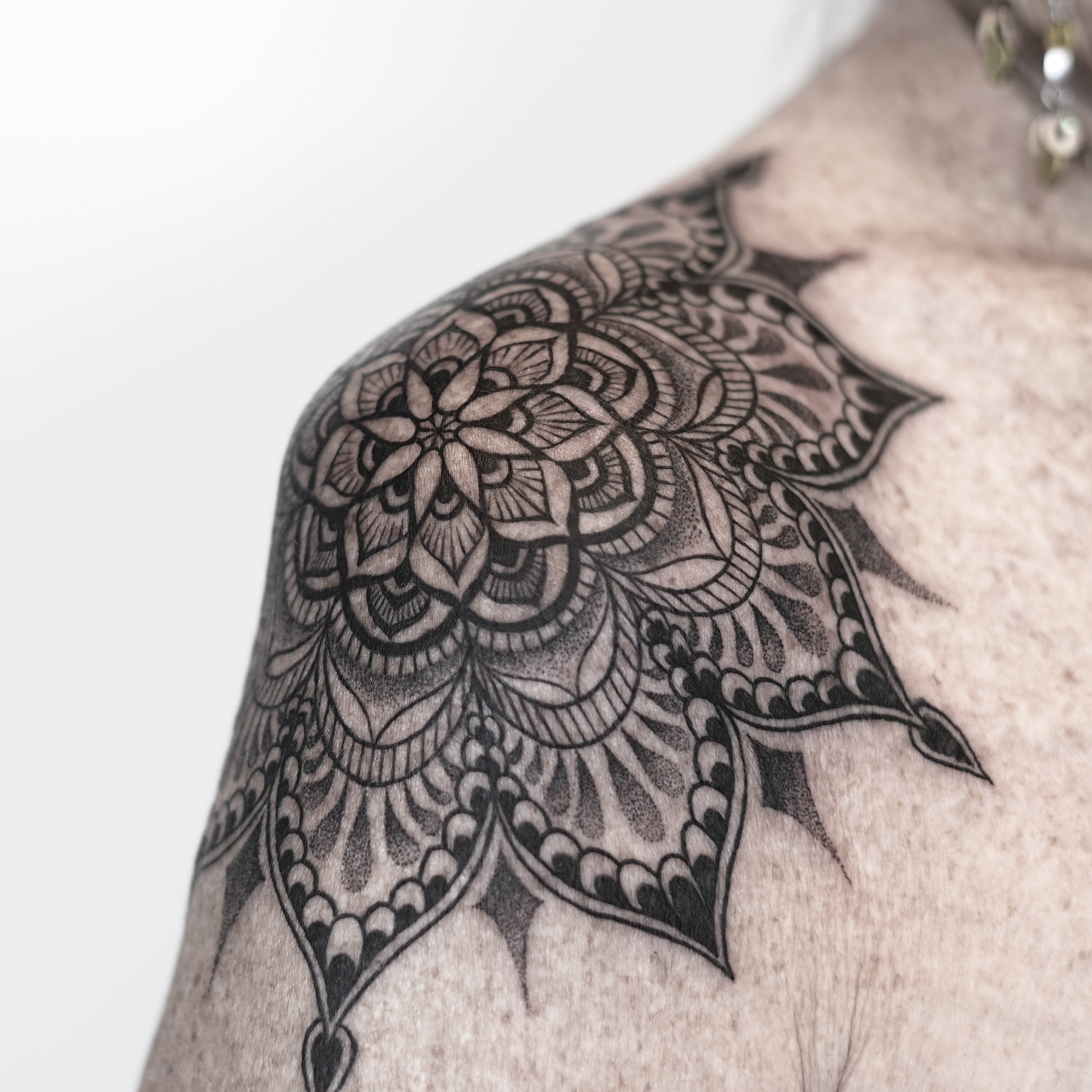 Intricate black mandala tattoo on shoulder with floral details
