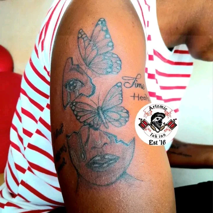 Black and grey butterfly and face portrait tattoo on upper arm