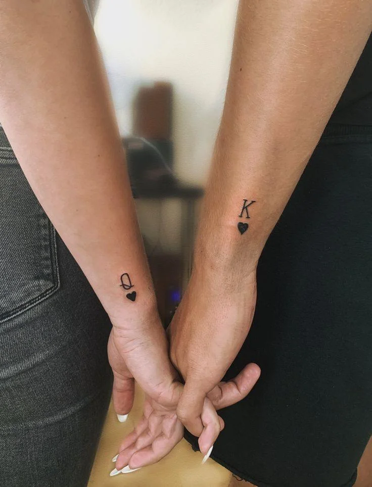 Matching minimalist playing card tattoos on forearms with heart symbols