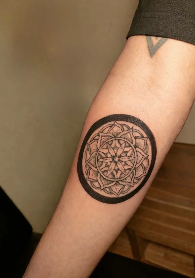 Black and grey mandala tattoo with circular border on forearm