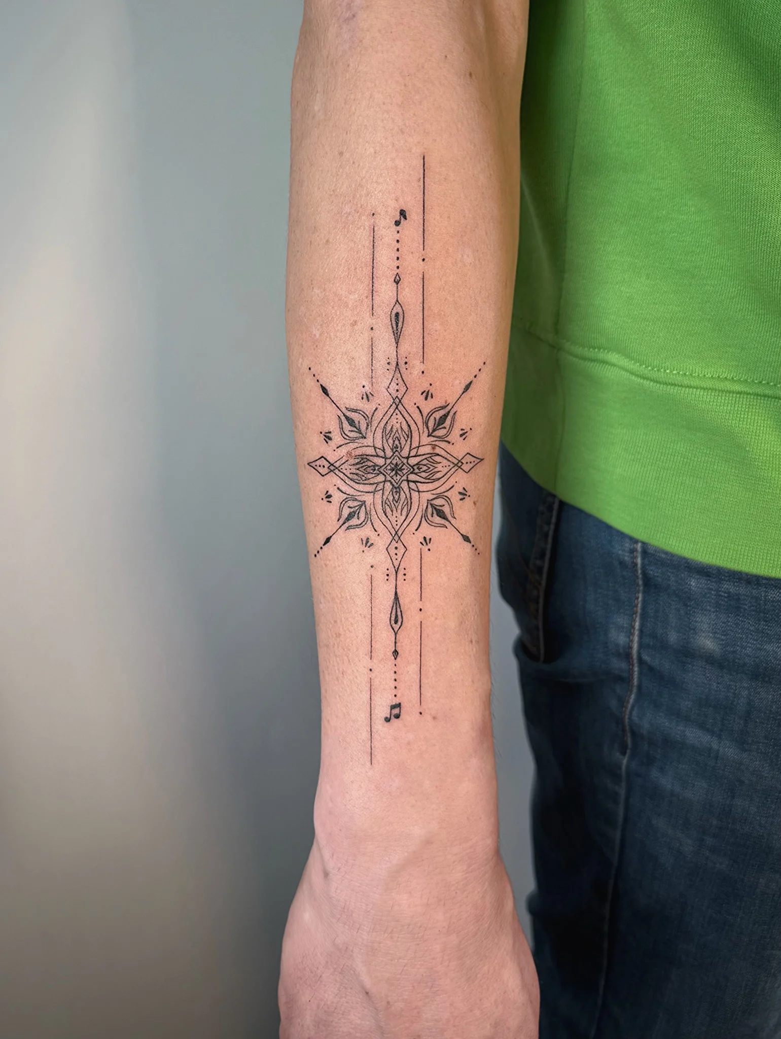 Fine line mandala lotus tattoo with music notes on forearm