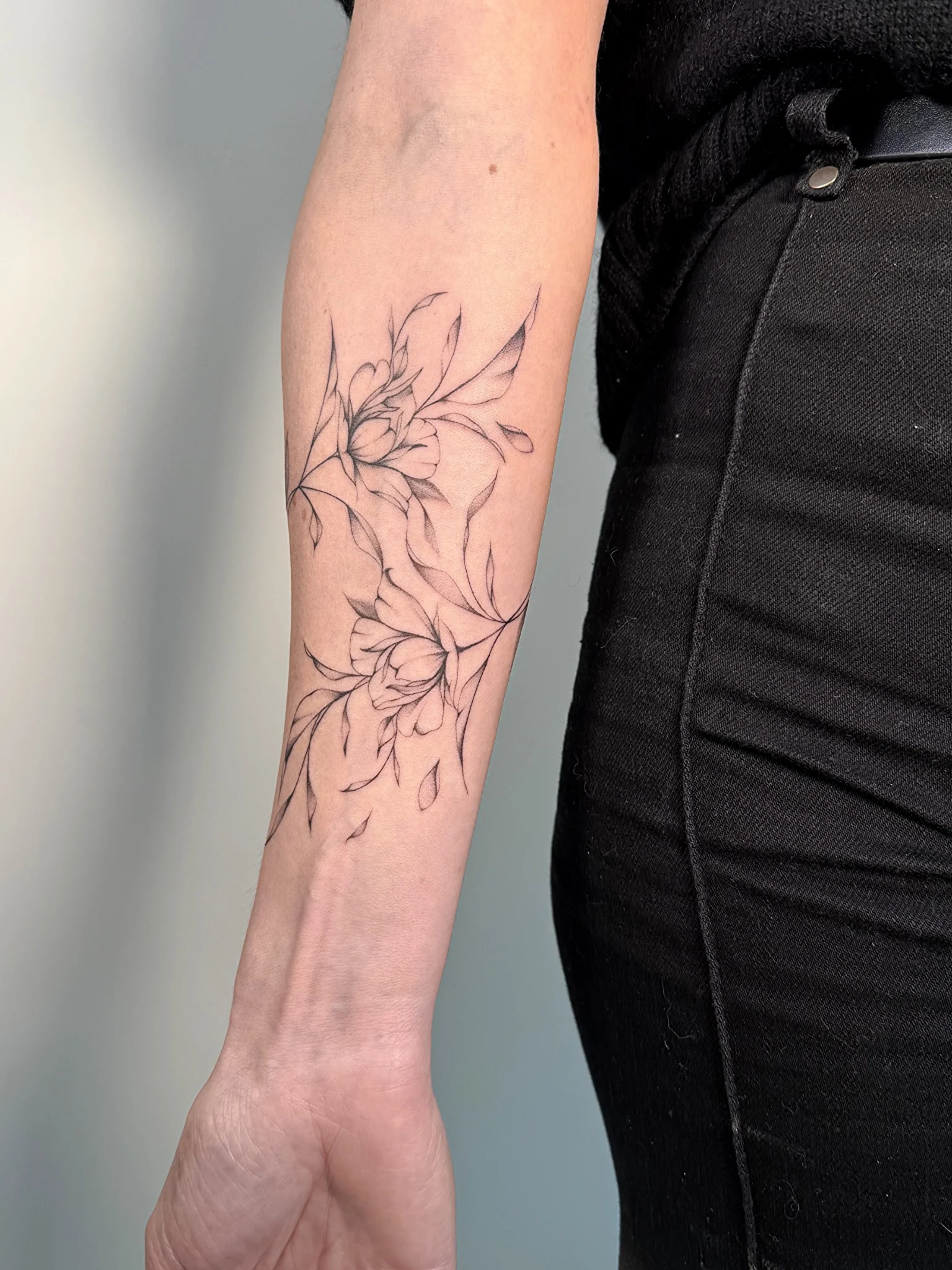Fine line floral botanical tattoo with leaves on forearm
