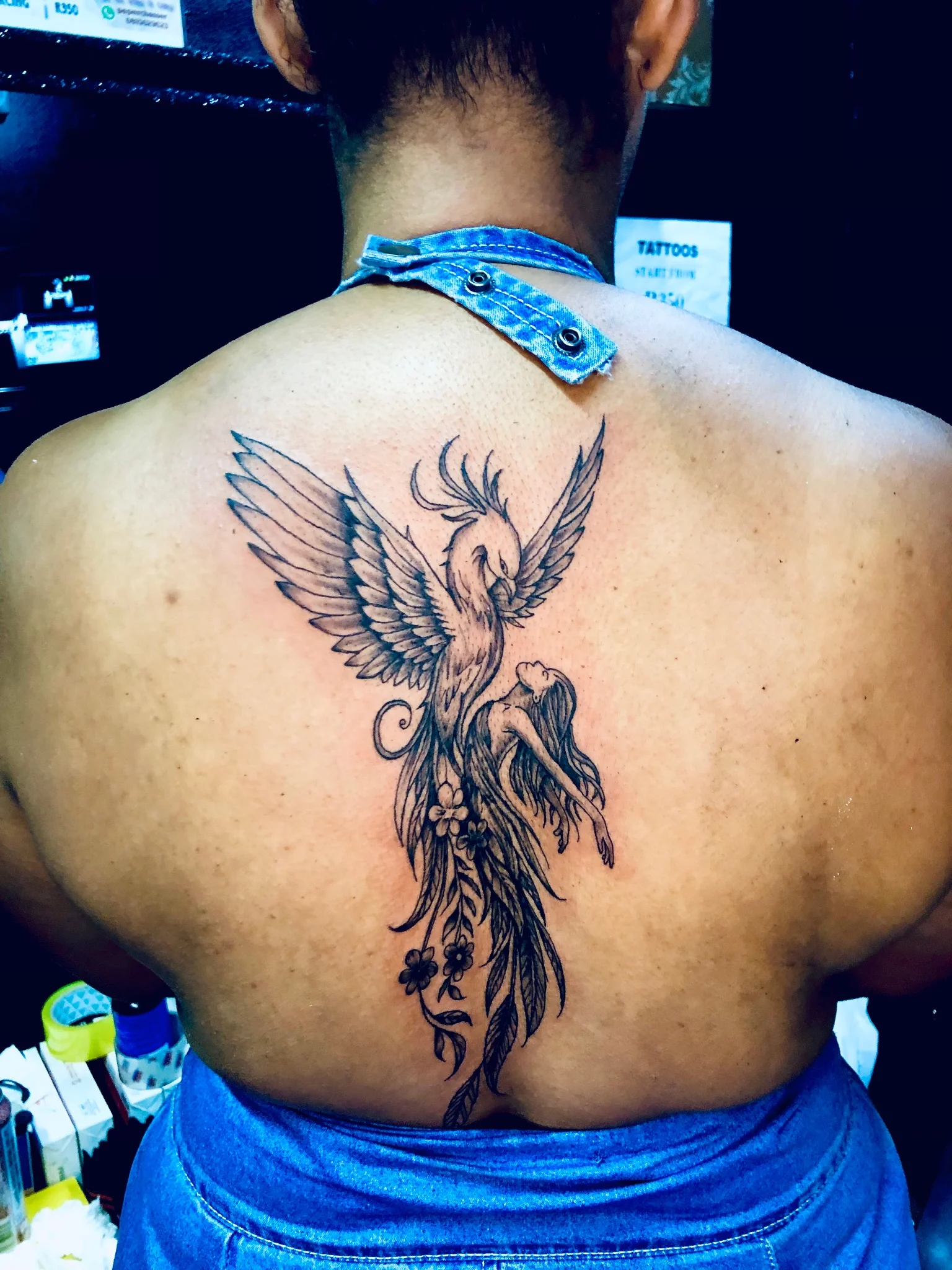 Black and grey phoenix tattoo on upper back with floral elements