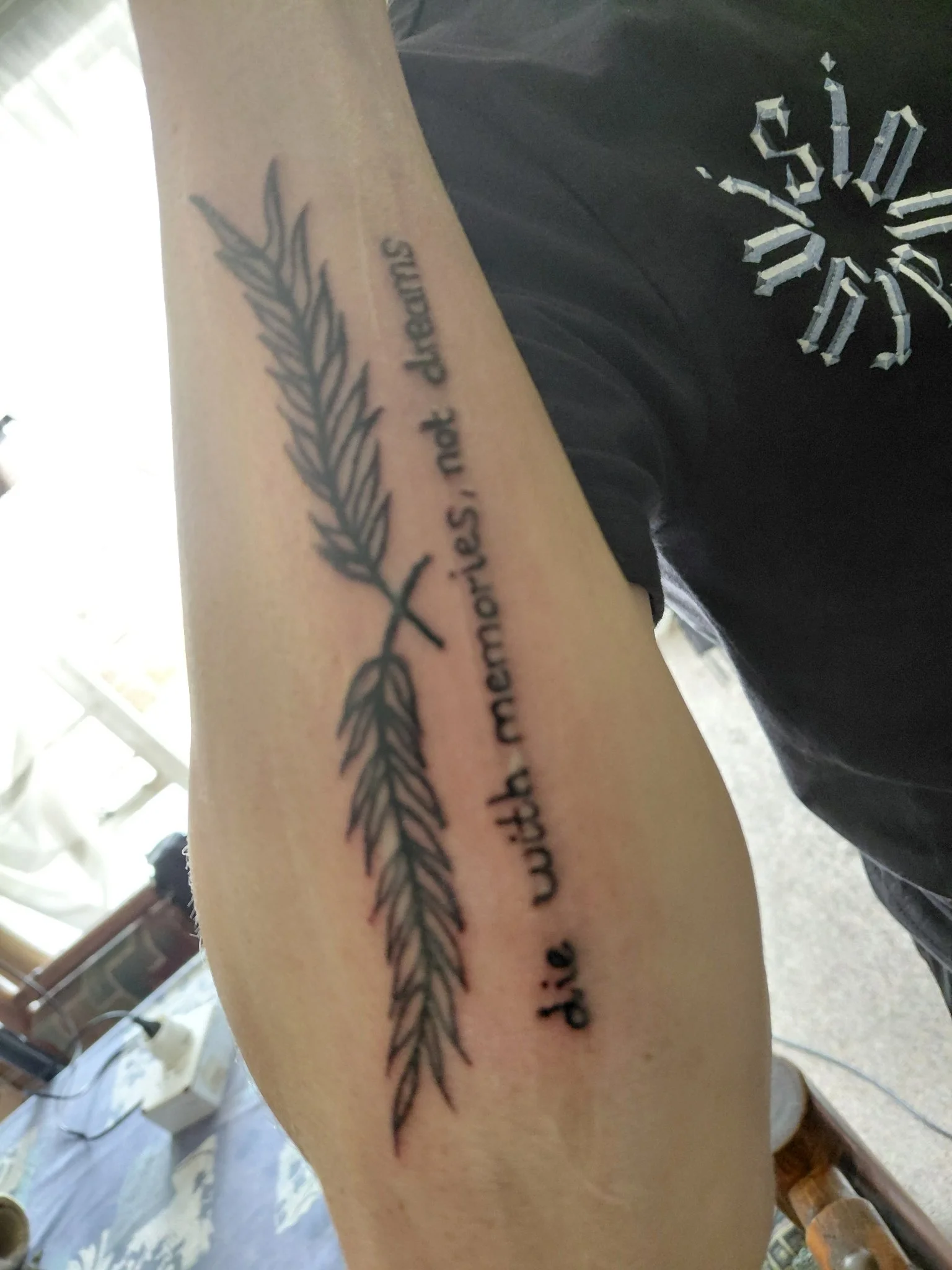 Black and grey feather with script text on forearm